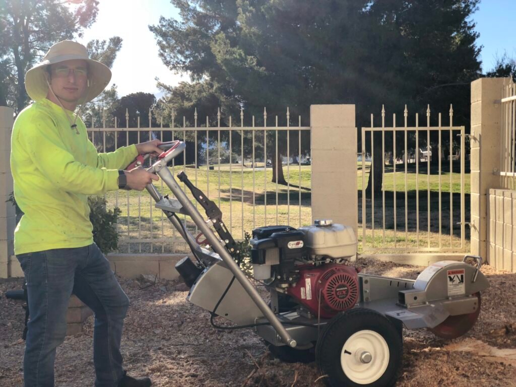 tree care worker looking at camera with stump grinder removing a large pine tree stump that is in the backyard of home